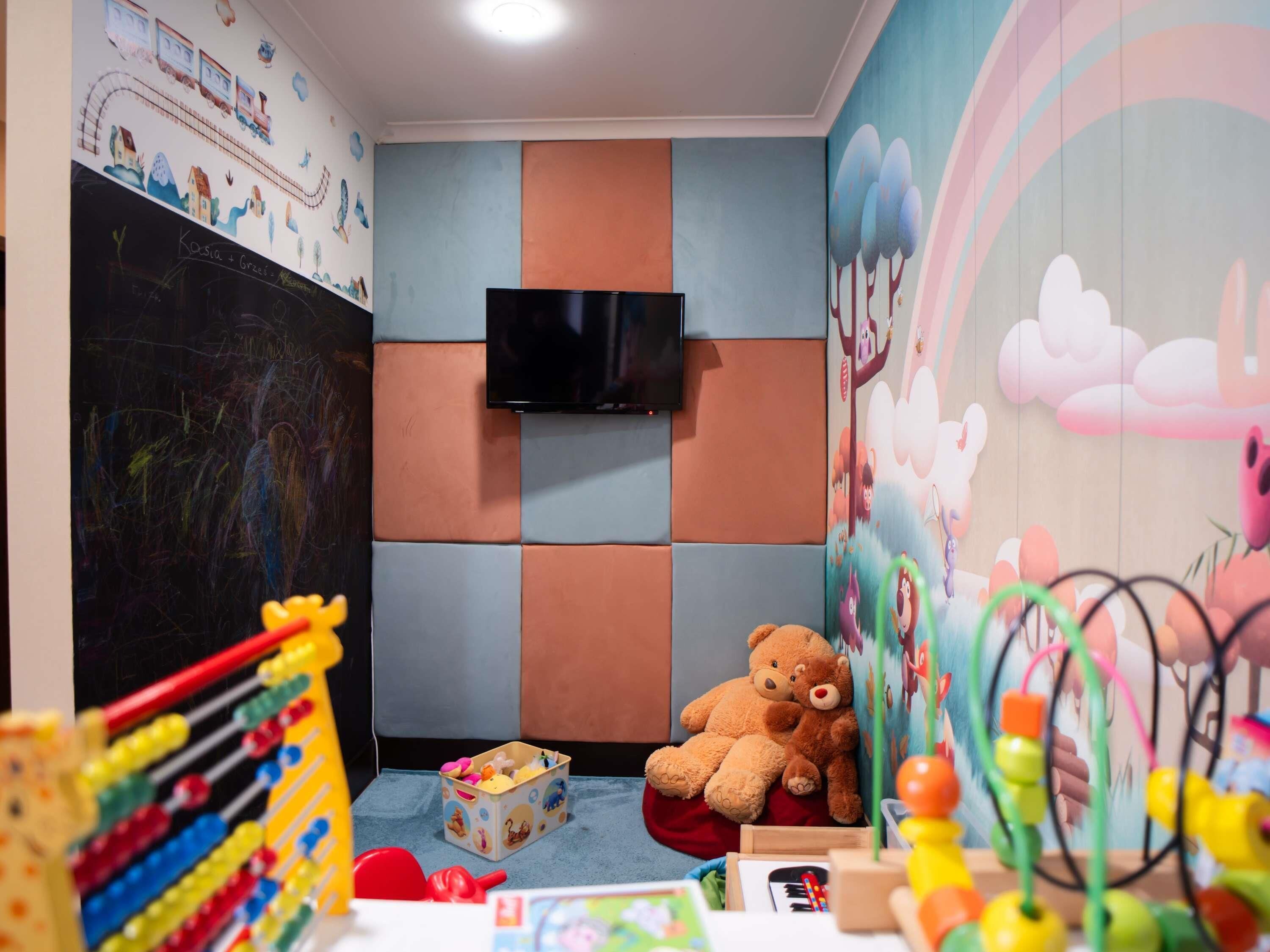 Una sala de juegos para niños con televisión, juguetes y un osito de peluche.