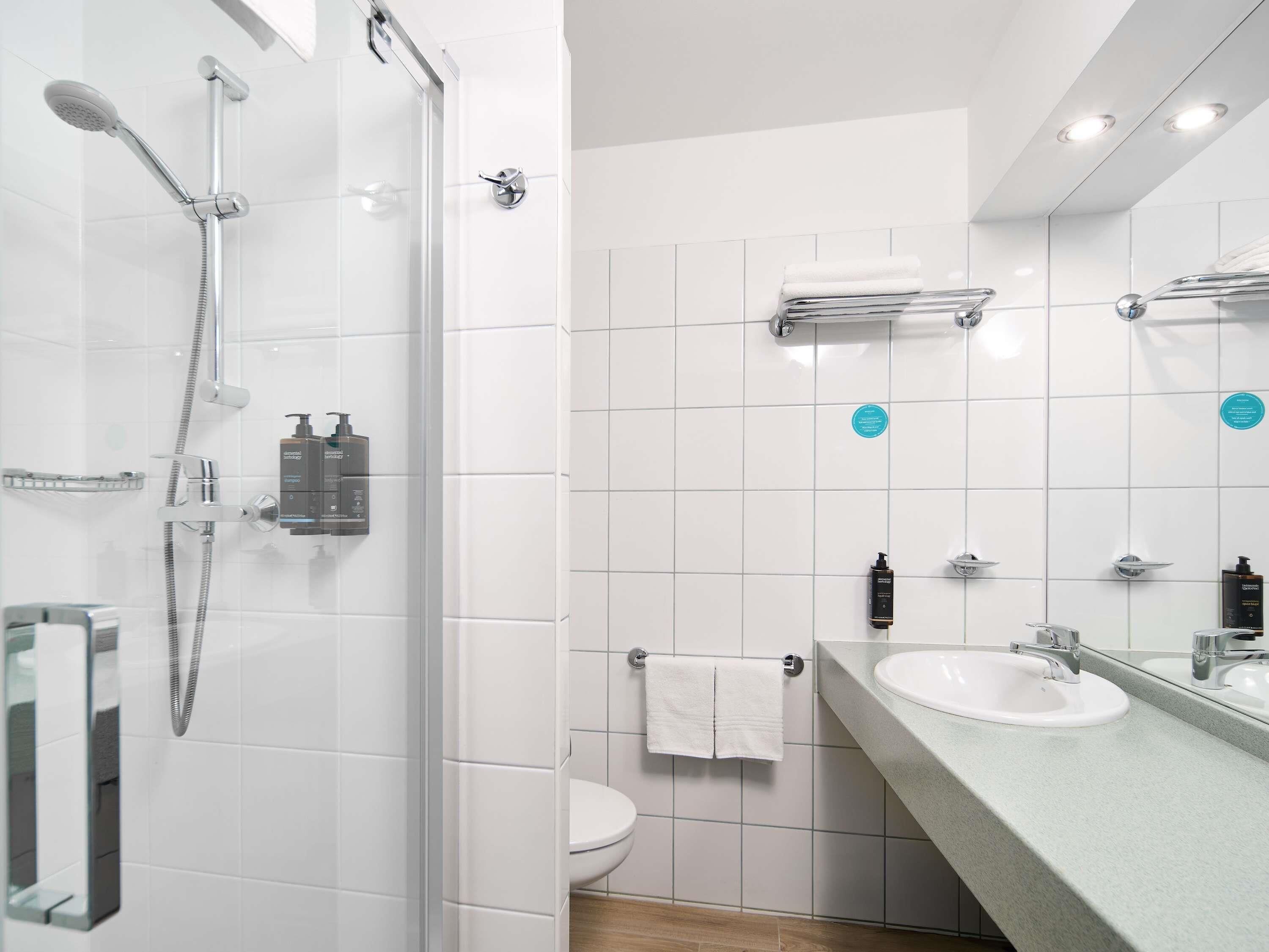 Un bany modern amb dutxa de vidre, un vàter blanc i un lavabo amb mirall.