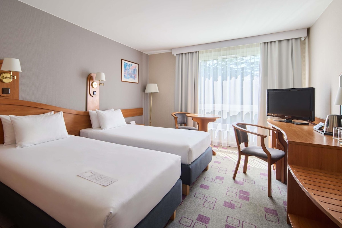 A hotel room with two beds, a desk with a television, and a window with curtains.