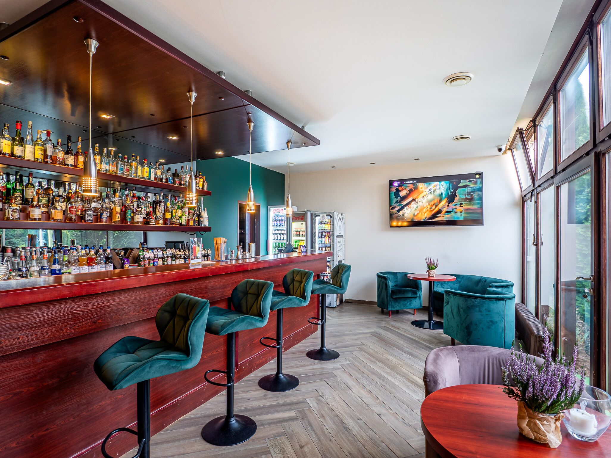 A bar area with a wooden bar counter, multiple liquor bottles, and green upholstered bar stools.