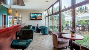 A modern bar area with seating, a large TV screen, and a view of the outdoors. - Mercure Cieszyn (Cieszyn)