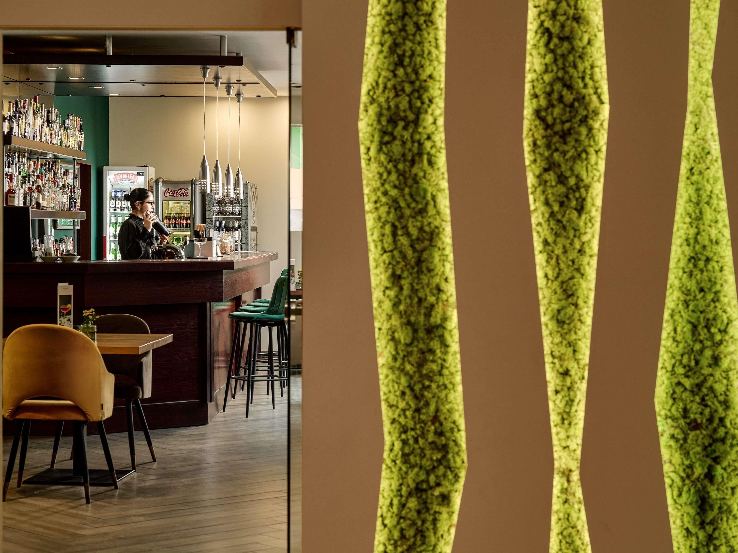 Uma área de bar com um bartender, prateleiras de garrafas e banquetas.