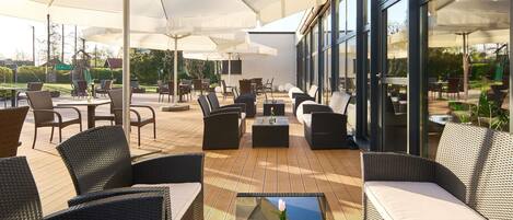 Une terrasse extérieure aménagée avec des meubles en osier, des tables en verre et des parasols.