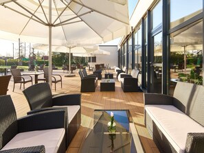 An outdoor patio with wicker furniture, glass tables, and umbrellas.