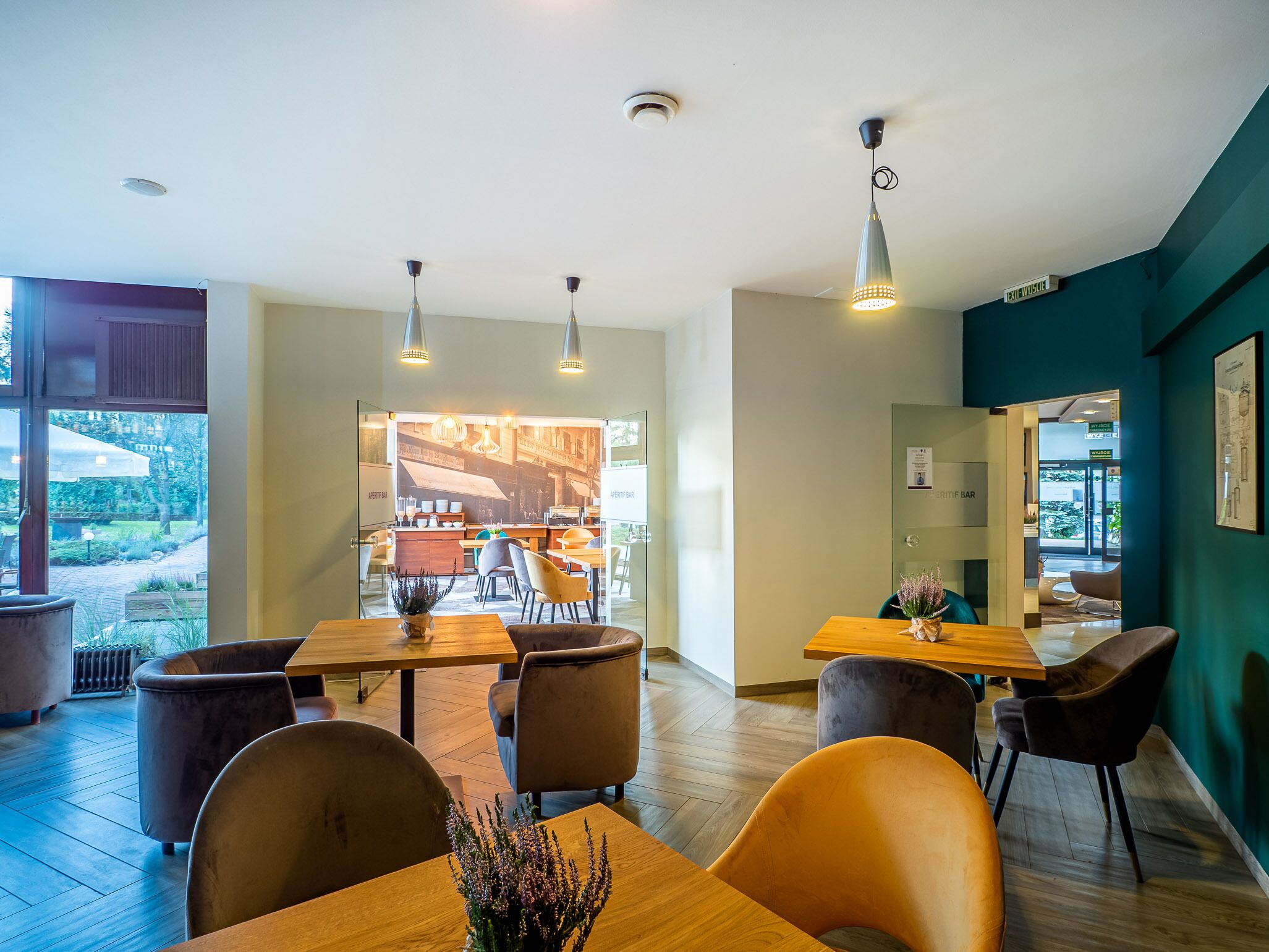A modern restaurant with wooden tables and chairs, pendant lighting, and a view of the outdoor seating area.