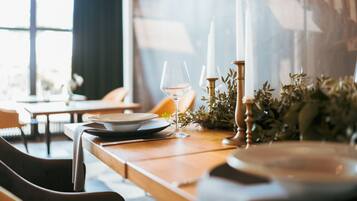 A dining table set with plates, a wine glass, and candles, with a view of a cityscape through a window.