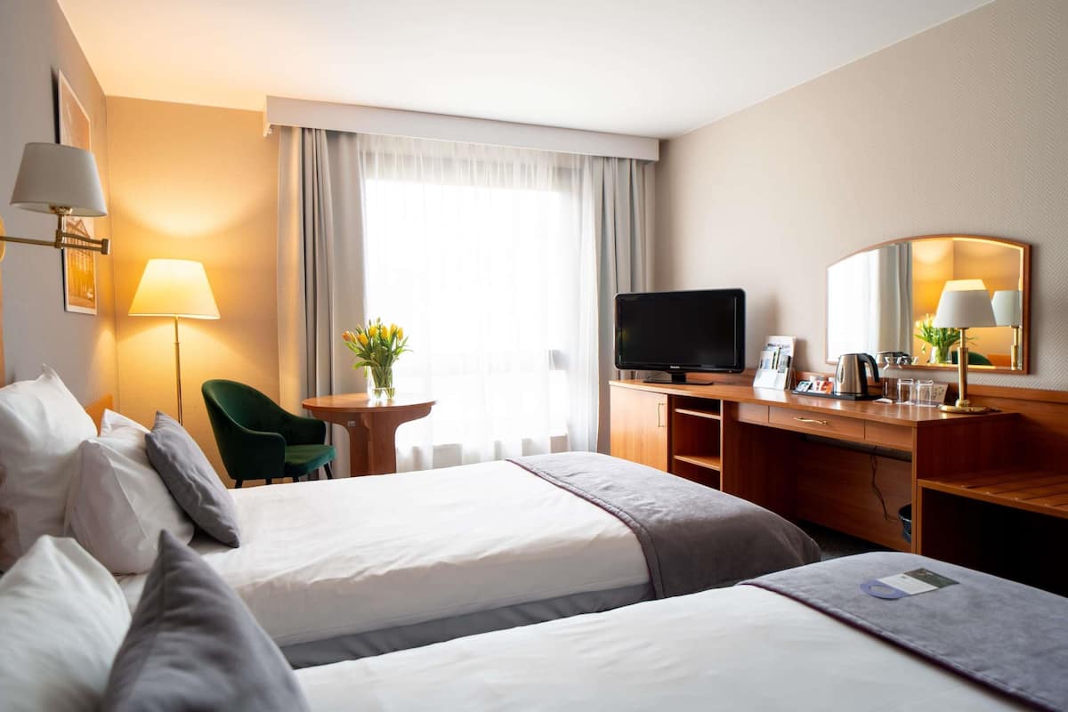 A hotel room with two beds, a desk, a television, a mirror, and a window with curtains.