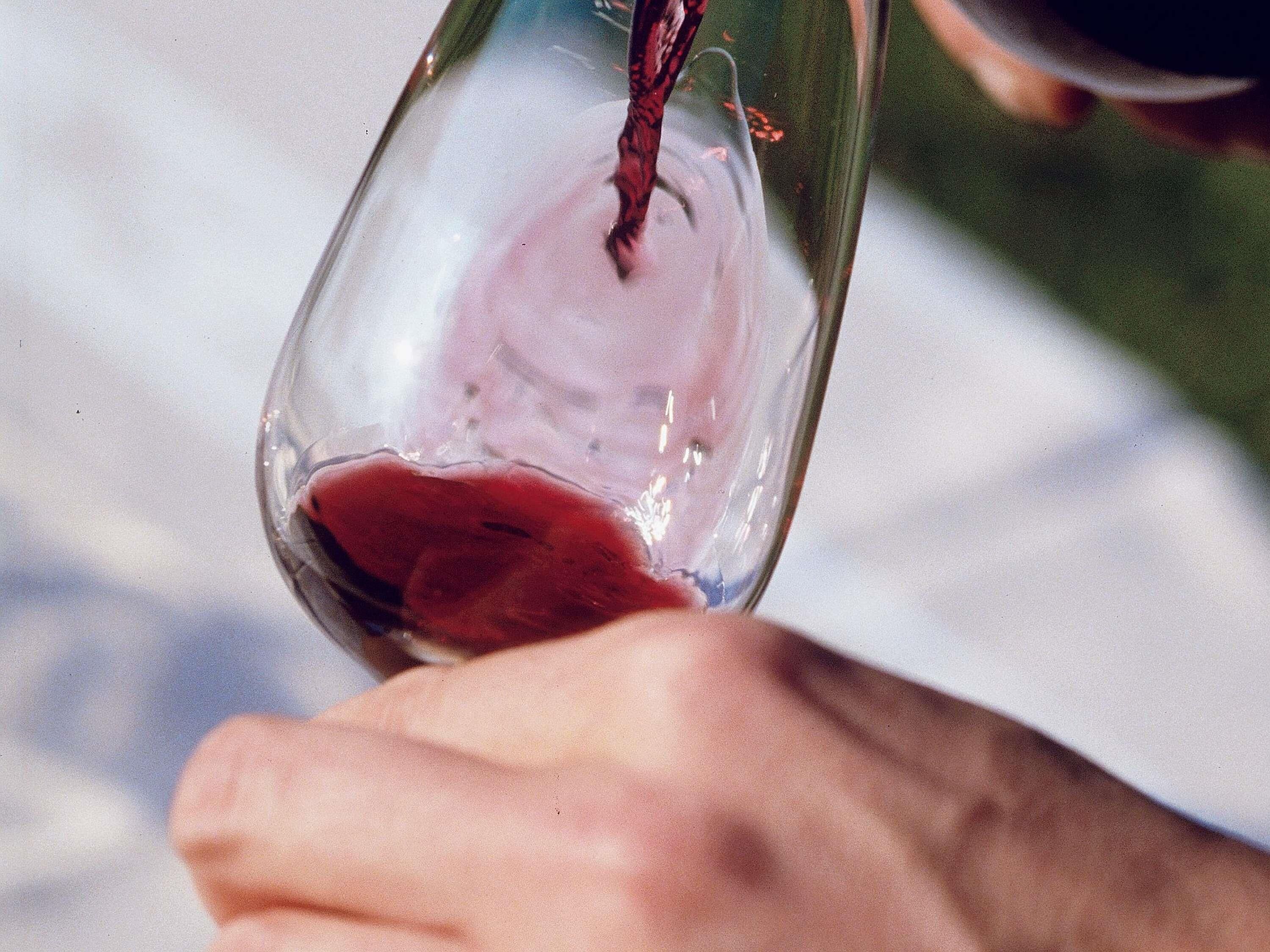 A hand holding a wine glass with red liquid.