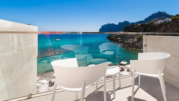 Un balcón con vistas despejadas al mar, con sillas y una mesa blancos.