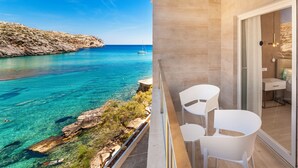 Un balcón con vistas despejadas al mar, una cama con colcha verde y una mesita con dos sillas.