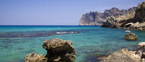 A rocky coastal landscape with clear blue waters and a large rock formation in the foreground.