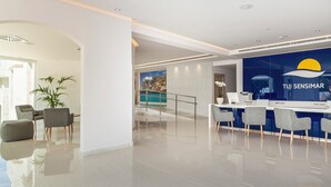 A modern hotel lobby with a reception desk, seating area, and a view of a pool.