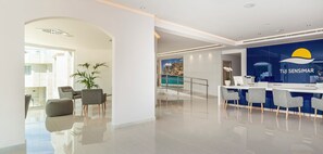 A modern hotel lobby with a reception desk, seating area, and a view of a pool. - Globales Don Pedro Adults Only +16 (Pollensa)