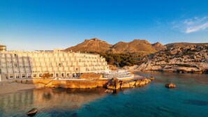Un hotel costero con varios balcones, un patio central y vistas del paisaje rocoso circundante y aguas azules cristalinas.