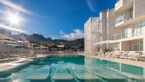 Zona de piscina con tumbonas y sombrillas, cielo despejado y montañas al fondo.