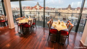 Un comedor con mesas y sillas, ventanas amplias con vistas a la ciudad y suelo de madera.