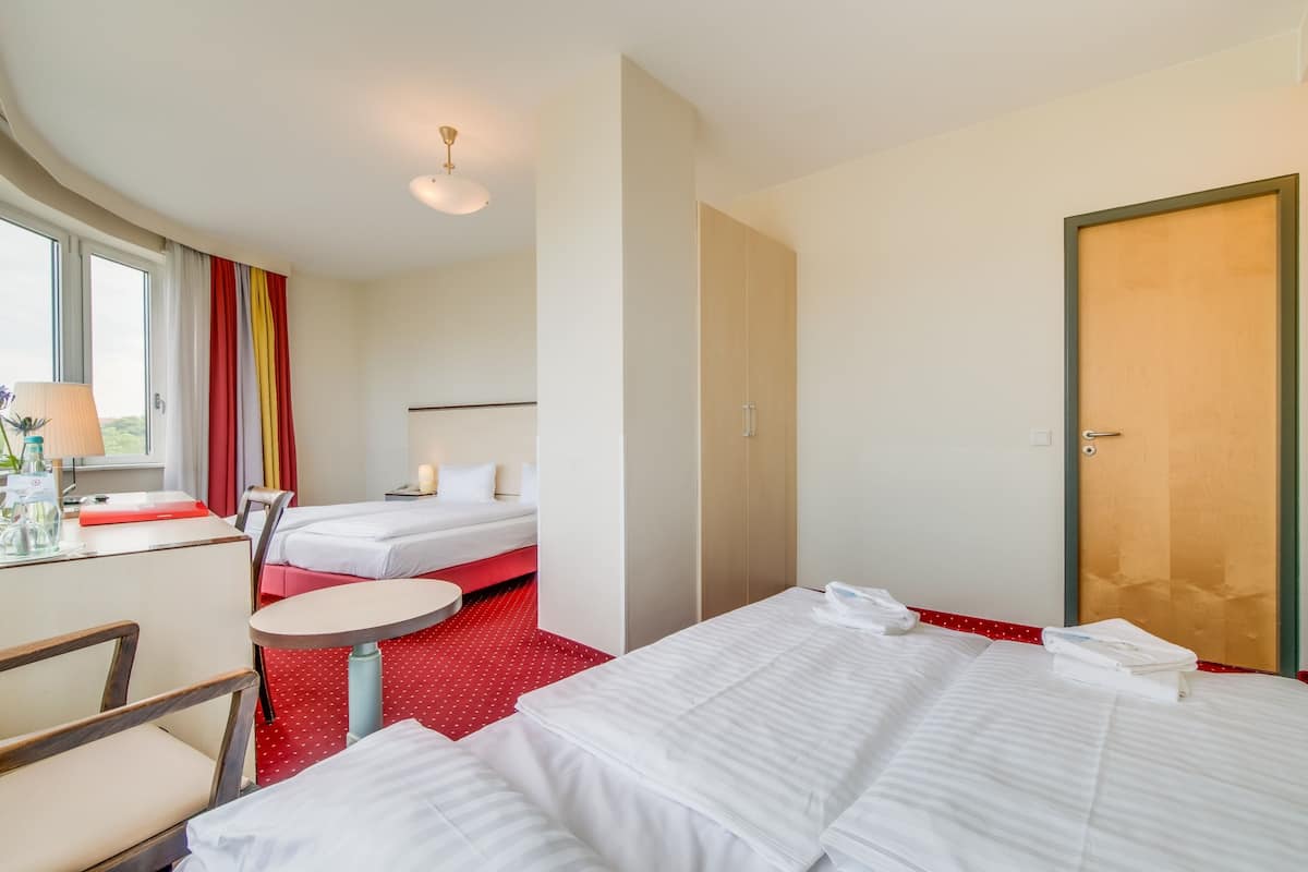 Ein Hotelzimmer mit zwei Betten, einem kleinen runden Tisch, einem Stuhl, einem Fenster mit Vorhängen und einer Tür.