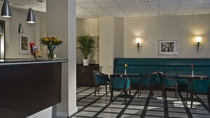 Un área de recepción con mostrador de registro, sillas color esmeralda, un sofá verde e iluminación en la pared.