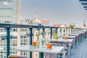 A balcony with tables and chairs, a clear view of buildings in the background, and a bottle of water on one of the tables. - Come Inn Berlin Kurfürstendamm (Berlin)