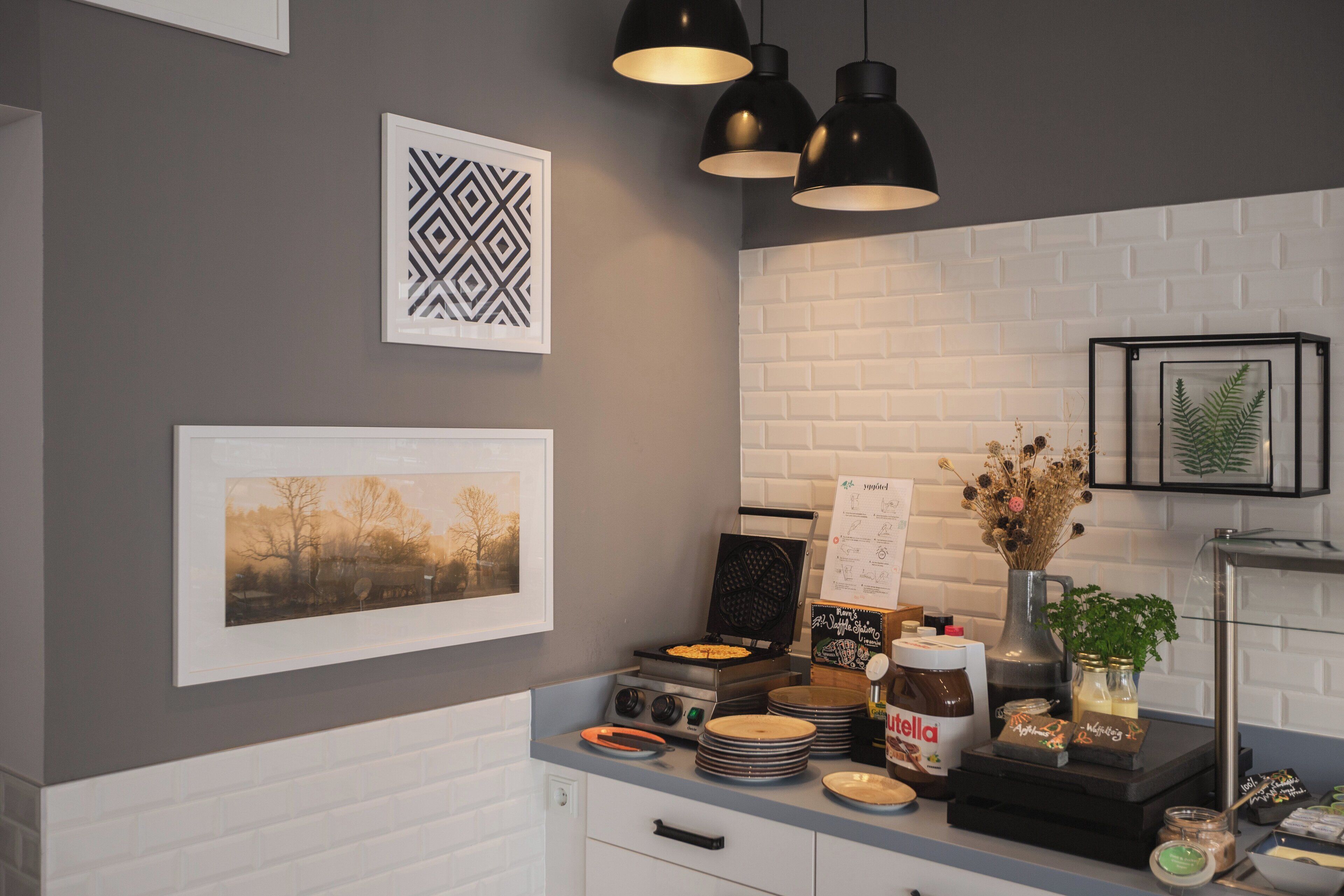 A kitchen with a white brick backsplash, black pendant lights, and various kitchen items on the counter.