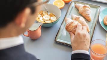 A breakfast setting with a bowl of cereal, croissants, a glass of orange juice, and a mug.