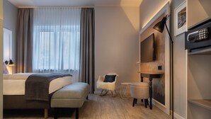 A hotel room with a bed, a chair, a small table, a floor lamp, and a TV mounted on the wall. - Garner Hotel Berlin - Wilmersdorf by IHG (Berlin)