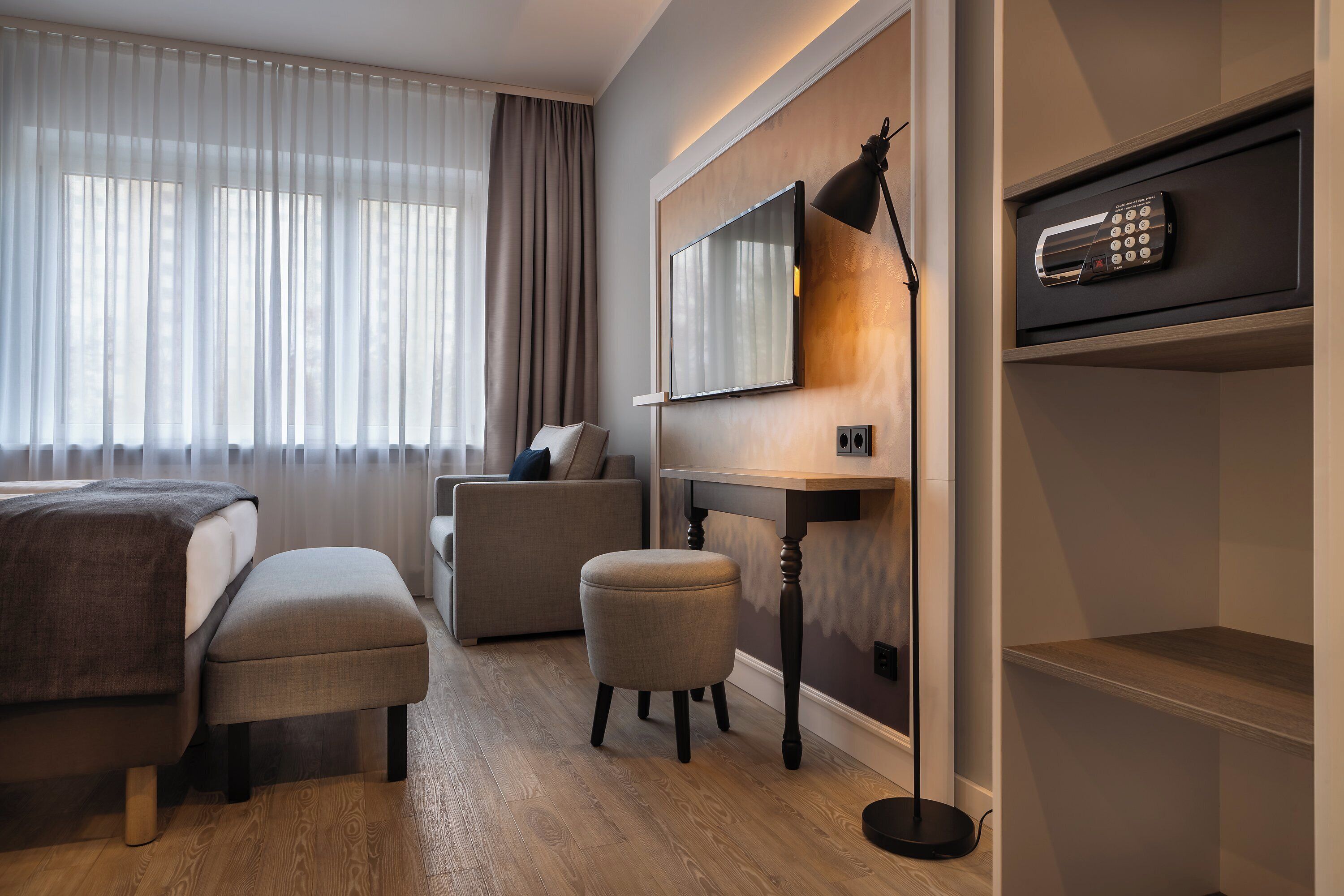 Ein Hotelzimmer mit einem Bett, einem Schreibtisch, einem Stuhl, einem Fernseher und einer Fernbedienung auf einem Regal.