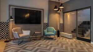 A modern interior with a large flat-screen TV, two chairs, pendant lighting, a radiator, and a patterned floor. - Garner Hotel Berlin - Wilmersdorf by IHG (Berlin)