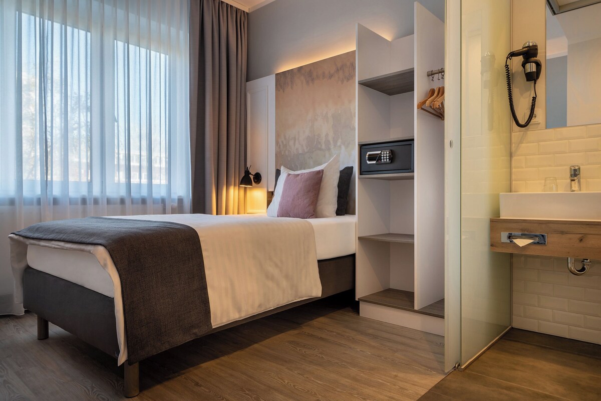 Una habitación de hotel moderna con cama, mesita de noche, estante empotrado con espejo y zona de ducha.