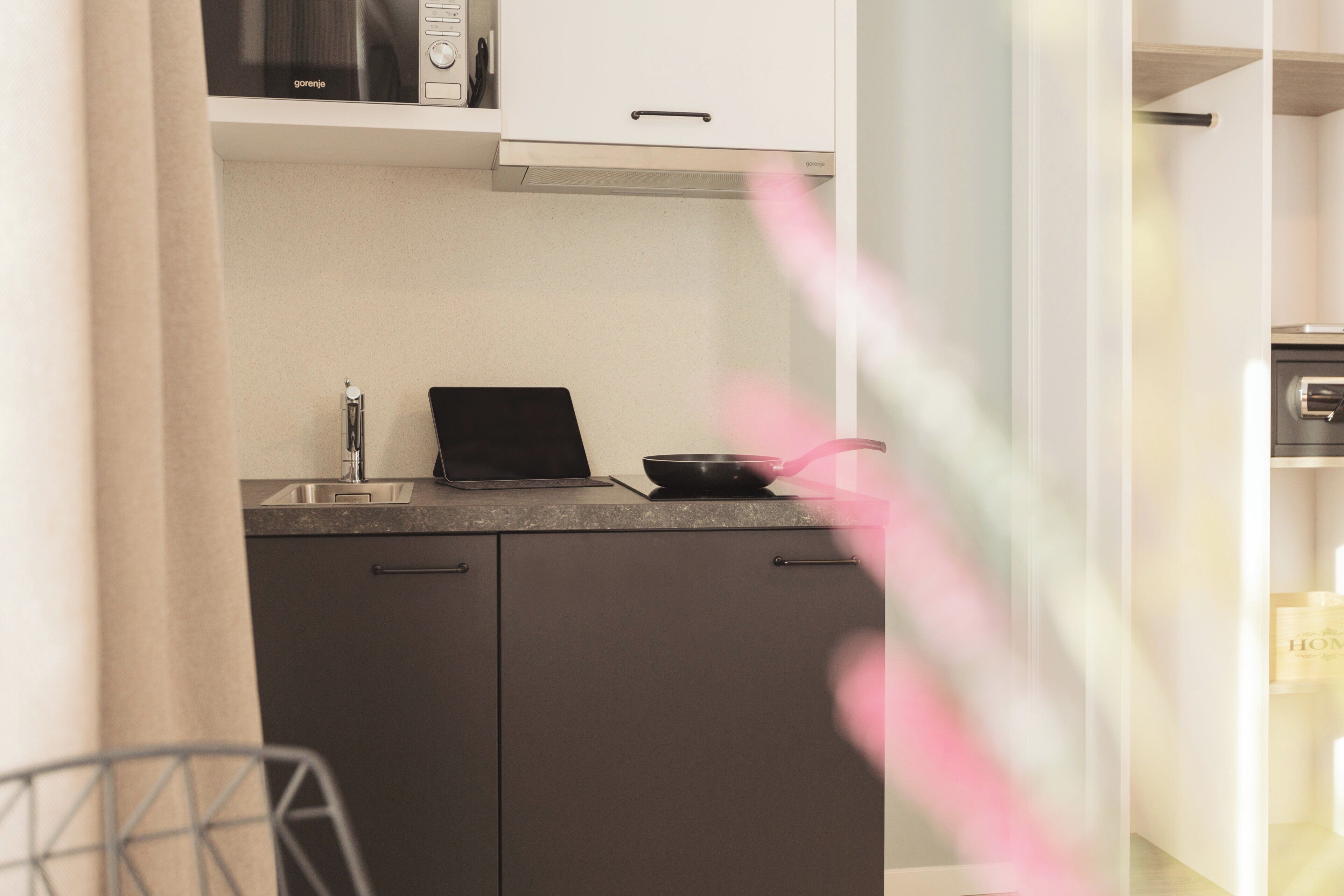 A modern kitchen with a microwave, a laptop, and a frying pan on the counter.