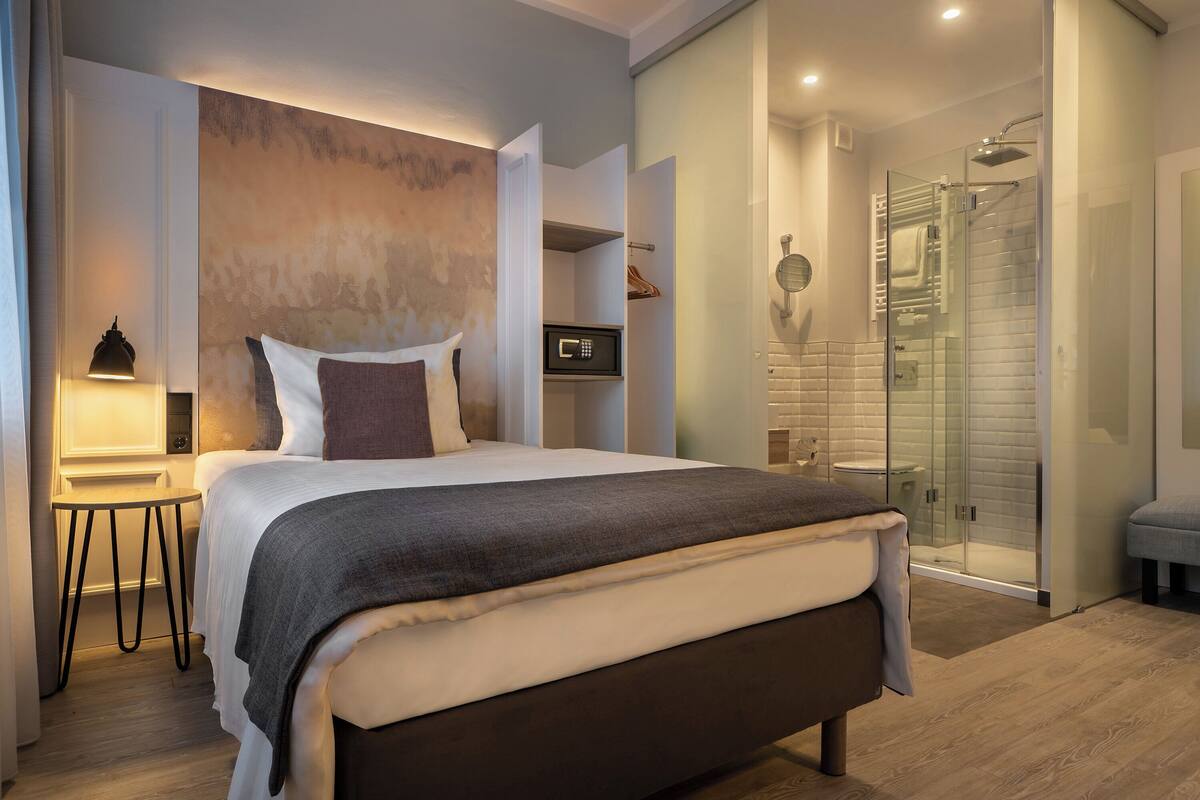 A modern bedroom with a large bed, bedside table, and a walk-in shower.