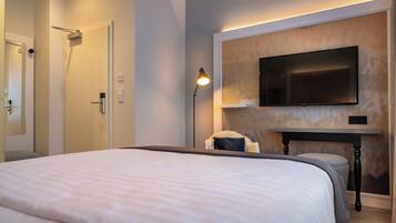 A modern hotel room with a large bed, a flat-screen TV mounted on the wall, a bedside table, and a nightstand.