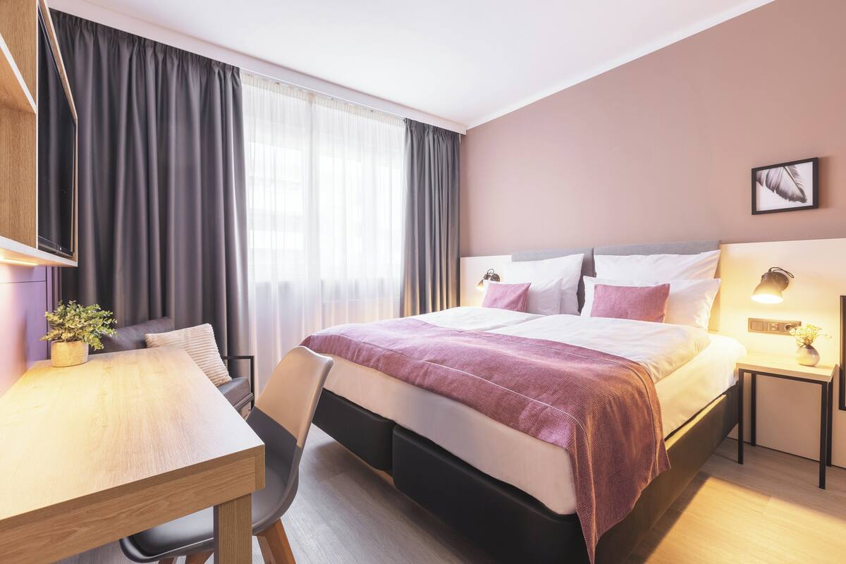 A modern hotel room with a large bed, a desk, and a chair.