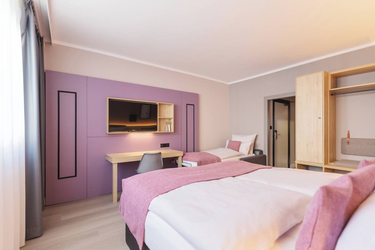 A hotel room with two beds, a desk, a chair, a wardrobe, and a mirror.