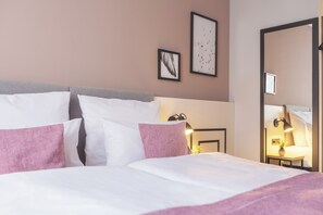 A neatly made bed with white and pink pillows, a bedside lamp, and a framed picture on the wall. - Garner Hotel Berlin Ku´Damm by IHG (Berlin)