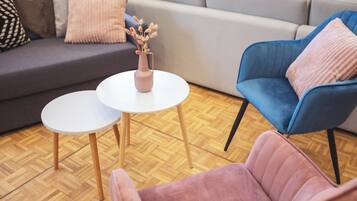 Un soggiorno moderno con un divano grigio, una poltrona blu e una poltrona rosa. Si nota un piccolo tavolino con un vaso di fiori secchi.
