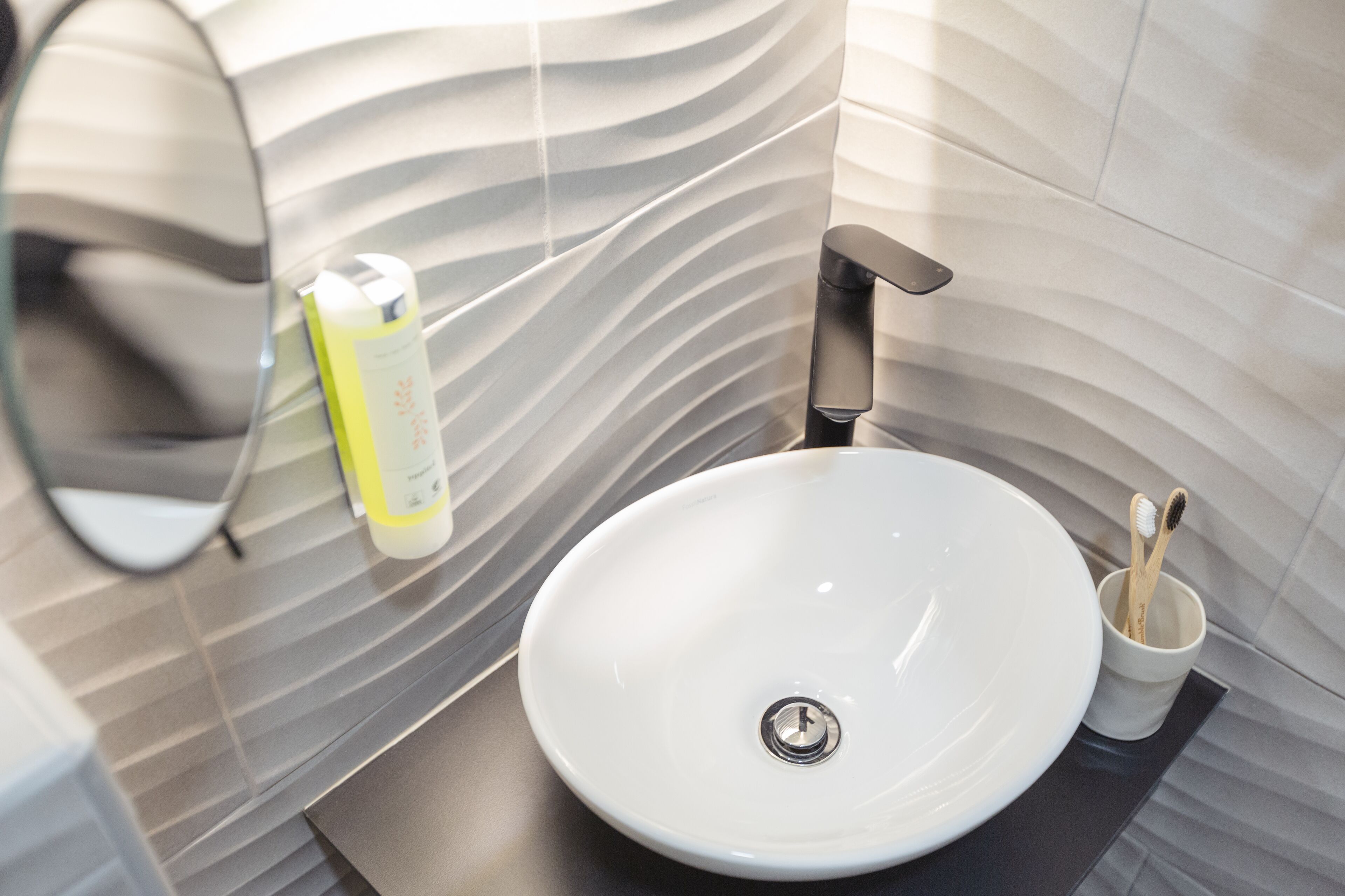 A modern bathroom with a white sink, a black faucet, and a mirror. There is a toothbrush holder with two toothbrushes.