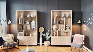 A modern living room with two wooden bookshelves, a round coffee table, two armchairs, and a large mirror on the wall.
