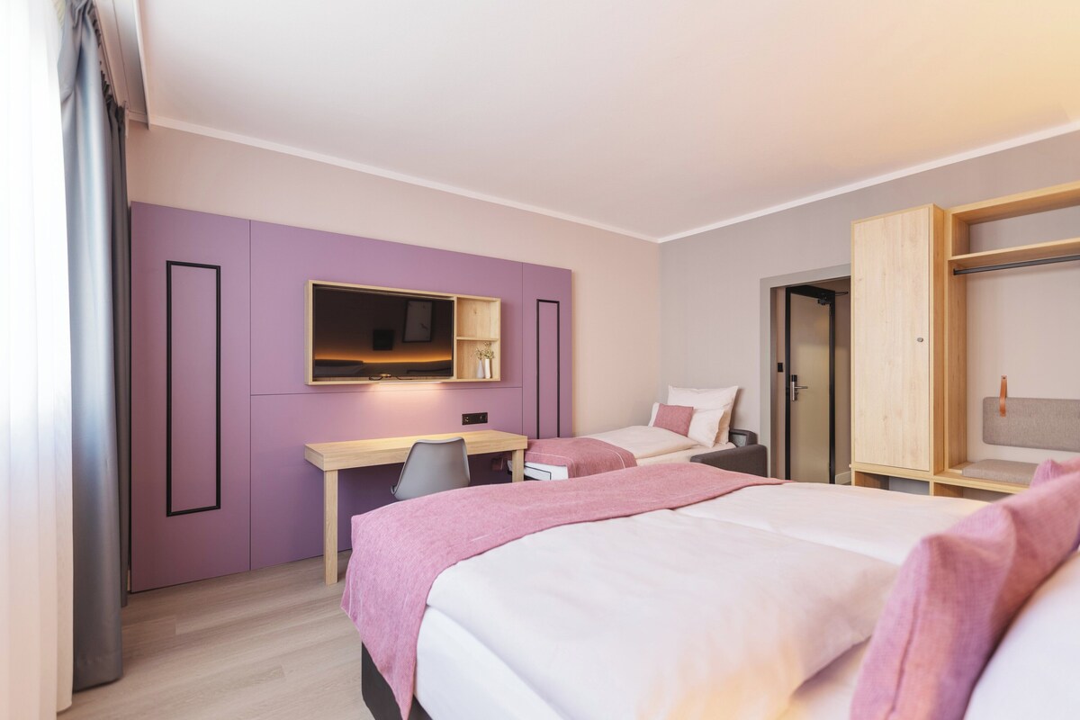 Habitación de hotel con dos camas, un escritorio, una silla, un armario y un espejo.