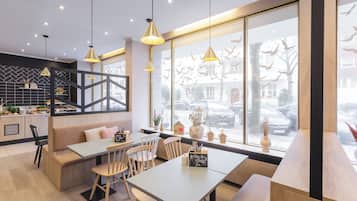 Una cafetería moderna con un amplio ventanal, muebles de madera e iluminación colgante.