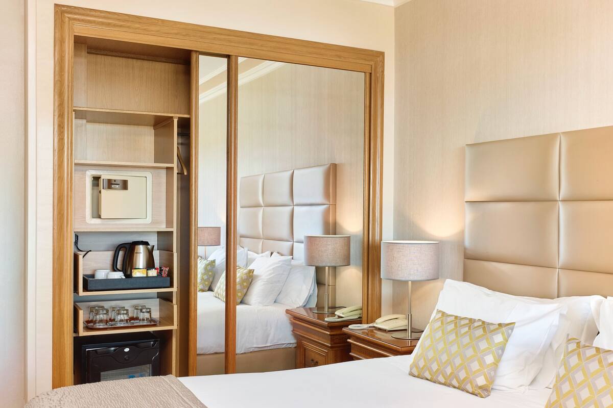 A hotel room with a bed, bedside tables, a wardrobe, and a mirror.