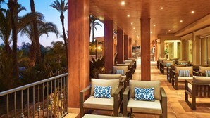 A covered outdoor seating area with wooden furniture and a view of palm trees. - Ria Park Hotel & Spa (Loulé)
