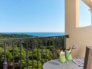 A balcony with a view of the sea, two green cocktails, and a newspaper on a table.
