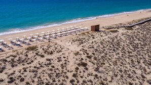 A beach with rows of sun loungers and umbrellas, a wooden walkway along the shore, and a small building on the sand. - Ria Park Hotel & Spa (Loulé)