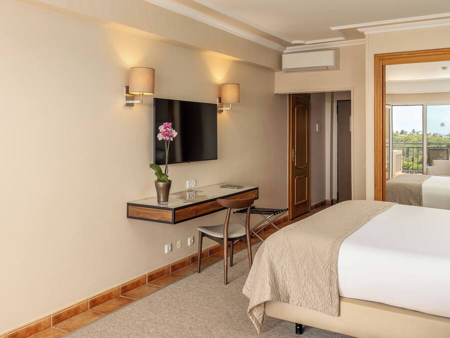 A hotel room with a bed, a desk with a chair, a flat-screen TV mounted on the wall, and a view of the outdoors.