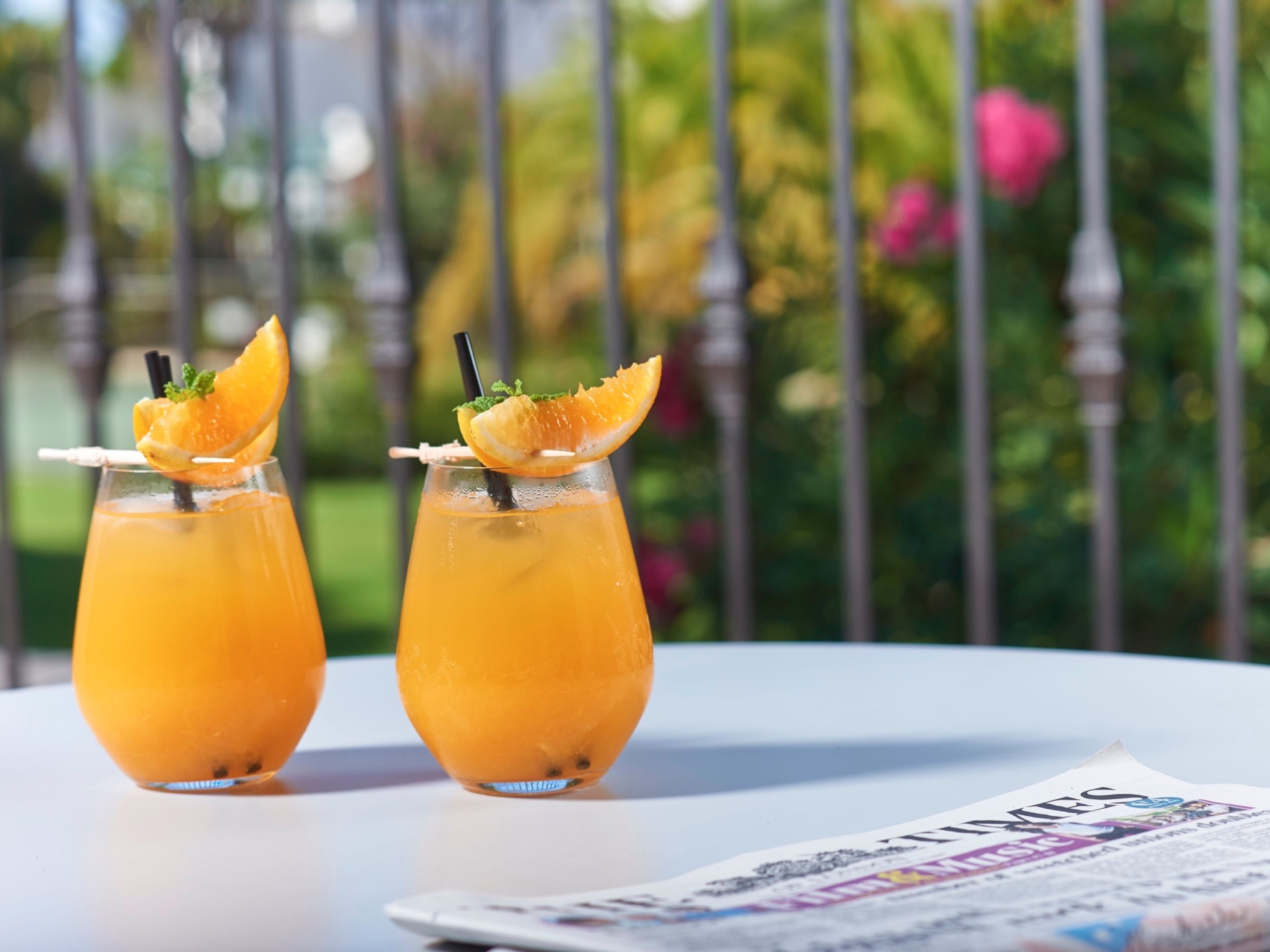 Two glasses of orange beverage on a white table with a newspaper.