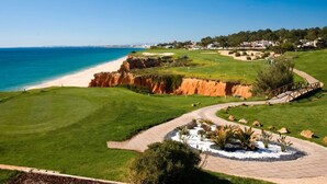 A golf course with a beach view, a paved pathway, and a landscaped area with plants. - Ria Park Hotel & Spa (Loulé)