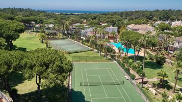 Vista aérea de um bairro residencial com várias quadras de tênis, piscina e vegetação exuberante.