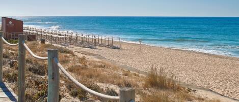 A beach with a wooden boardwalk leading to a row of sun loungers and a sign for RIA PARK HOTELS.