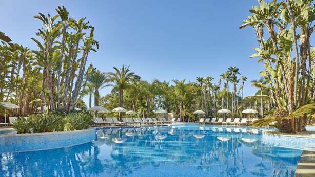 A swimming pool with tiled edges, surrounded by lounge chairs and umbrellas, with palm trees in the background. - Ria Park Hotel & Spa (Loulé)